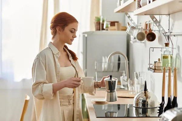 Uma bela mulher ruiva desfruta de sua rotina matinal, preparando café em uma cozinha brilhante. — Fotografia de Stock