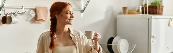 Sunlight brightens the kitchen as a red haired woman smiles, savoring her joyful drink. — Stock Photo