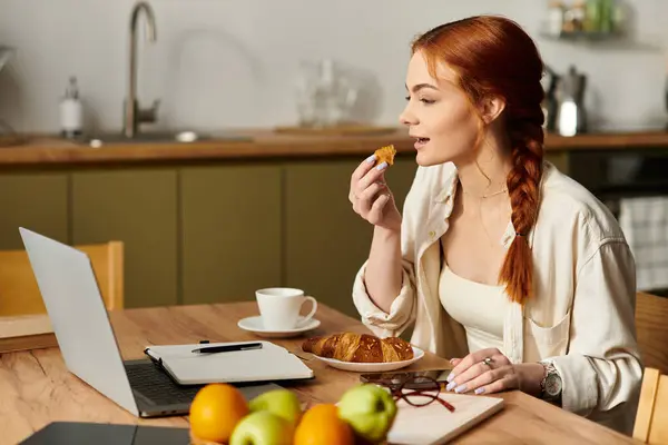 Bright morning as a woman with red hair savors a pastry and sips coffee while working at home. — Stock Photo