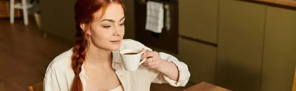 Woman with stunning red hair savors warm coffee in a peaceful kitchen ambiance while relaxing. — Stock Photo