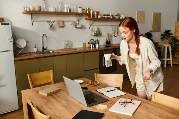 Une femme rousse aime le café et se régale à sa table en bois tout en travaillant. — Photo de stock