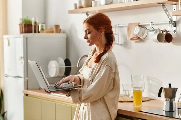 Brightly lit kitchen with a woman focusing on her laptop while enjoying a refreshing drink. — Stock Photo