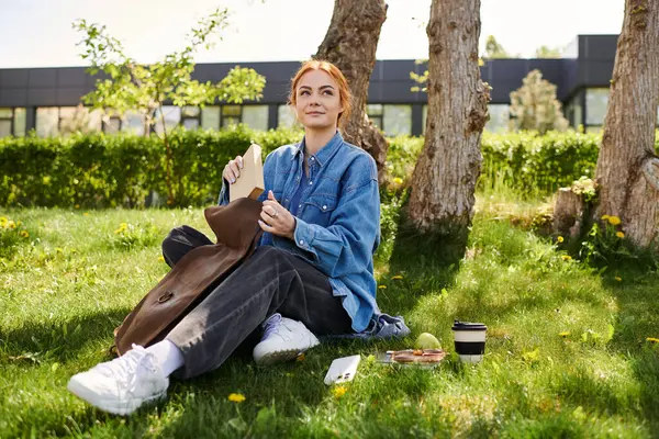 Red haired woman smiles as she unpacks food on the grass in a sunny park. — Stock Photo