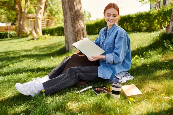 A red haired woman sits on the grass, creating amidst nature. — Stock Photo