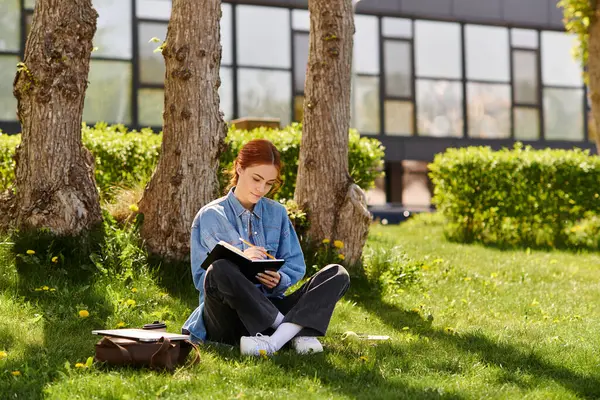A beautiful woman with red hair sits on the grass, writing thoughtfully while basking in sunlight. — Stock Photo