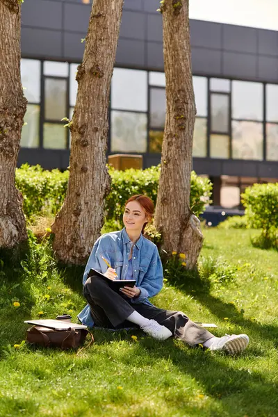 A red haired woman sketches on the grass under trees on a sunny day. — Stock Photo