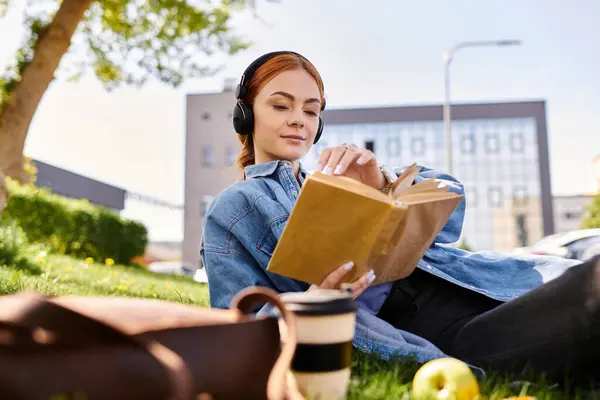 A serene moment unfolds as a red haired woman relaxes on the grass, engrossed in a book. — Stock Photo