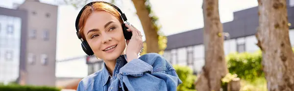 Uma mulher com belos sorrisos de cabelo vermelho enquanto imerso em música fora durante o dia. — Fotografia de Stock