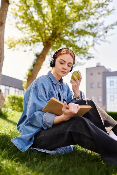 Eine rothaarige Frau entspannt sich draußen und schreibt in ihr Notizbuch, während sie einen grünen Apfel genießt. — Stockfoto