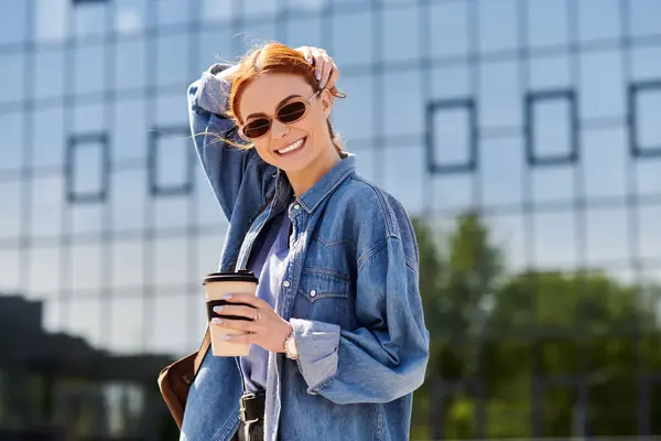 A radiant red haired woman laughs while holding a coffee cup, basking in the warm sun. — Stock Photo