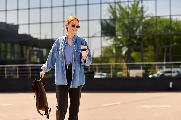A happy woman with red hair strolls outside holding a coffee cup in the sun. — Stock Photo