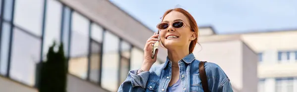 Bright sunny day finds a joyful woman with red hair conversing on her phone outdoors. — Stock Photo