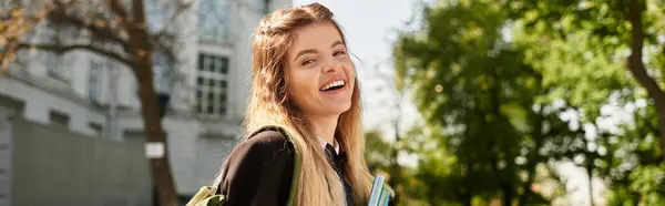 A pretty college girl in a stylish uniform carries books and smiles brightly while walking outdoors, banner — Stock Photo