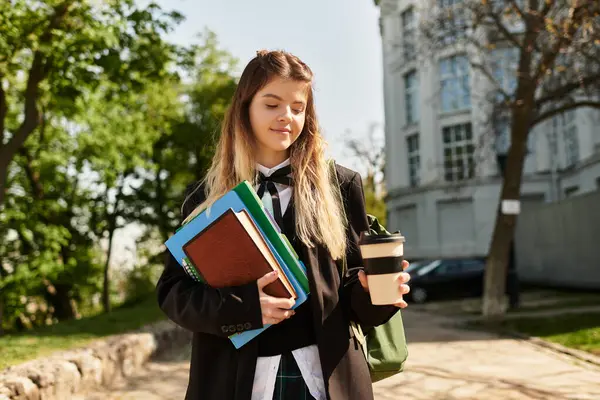 A college student strolls through a green campus, content with books and coffee in hand. — Stock Photo