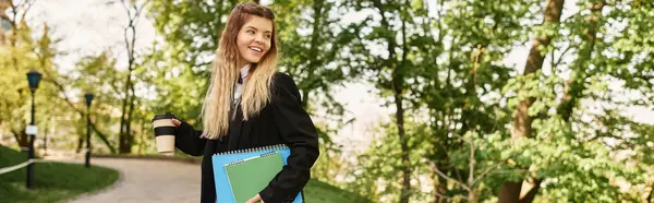 Giovane adulto in elegante uniforme universitaria gode di una passeggiata nel parco, tenendo un caffè e quaderni, banner — Foto stock