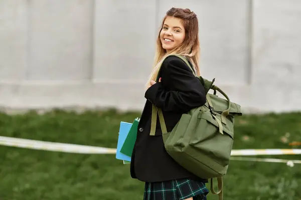 Adulto joven en un uniforme de moda disfruta de un momento en el campus, llevando libros y una bolsa. - foto de stock
