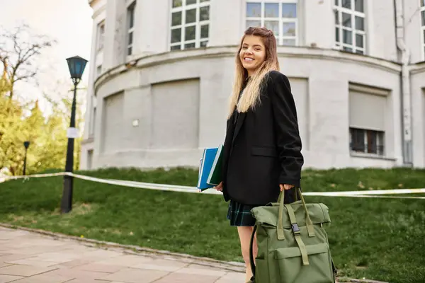 Young adult woman carries books and a backpack, showcasing her stylish uniform on campus. — Stock Photo