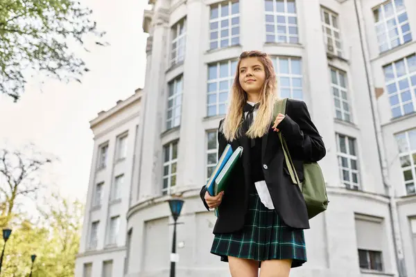 A pretty college girl in uniform carries books while enjoying a sunny day on campus — Stock Photo