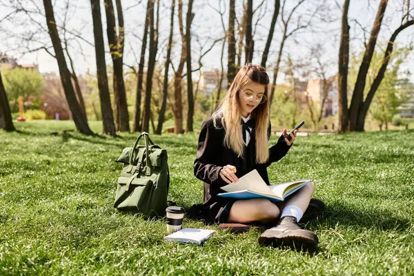 A pretty student relaxes on the grass while studying with her notes and using her phone outdoors. — Stock Photo