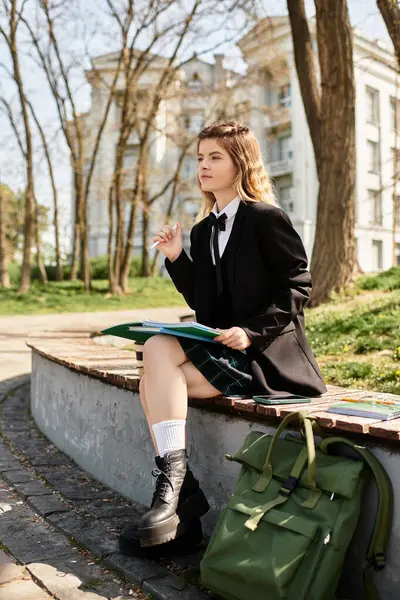 Pretty college girl in a stylish uniform sits on a bench, focused on her studies in the sun. — Stock Photo