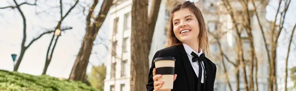 A young college student smiles brightly while savoring a cup of coffee outdoors on campus, banner — Stock Photo