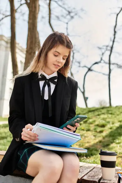 Un giovane adulto in un'uniforme alla moda del college si impegna con il suo telefono mentre studia all'aperto. — Foto stock