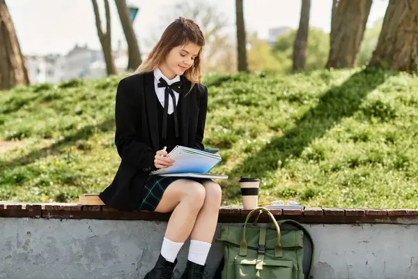 Studente universitario in uniforme studia con caffè e quaderni in un parco soleggiato. — Foto stock
