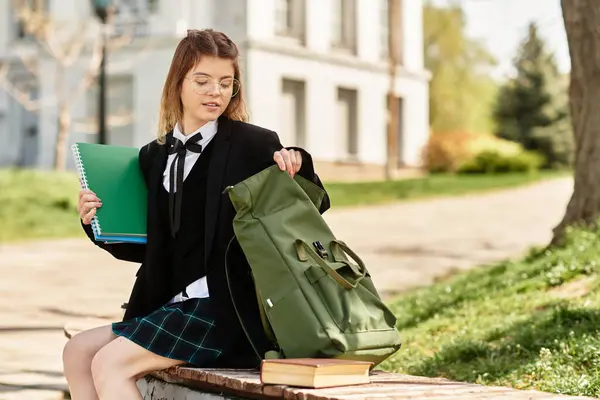 A pretty college student in uniform organizes her backpack while seated outside. — Stock Photo