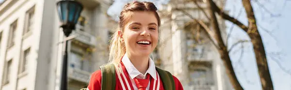 Молодая студентка колледжа излучает радость, когда идет по кампусу в яркой куртке подрывника, баннере — стоковое фото