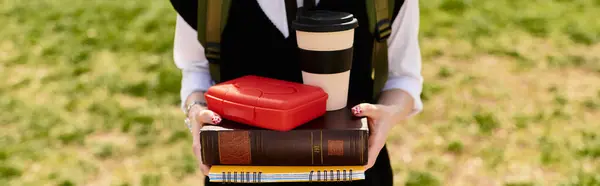 A young adult in a chic outfit stands on campus, balancing books and coffee, banner — Stock Photo