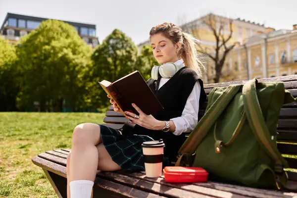 Stylish college student reads a book on a sunny day, surrounded by lush greenery in a park. — Stock Photo