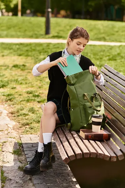 A young adult in a fashionable outfit organizes her bag while enjoying the park's serene atmosphere. — Stock Photo