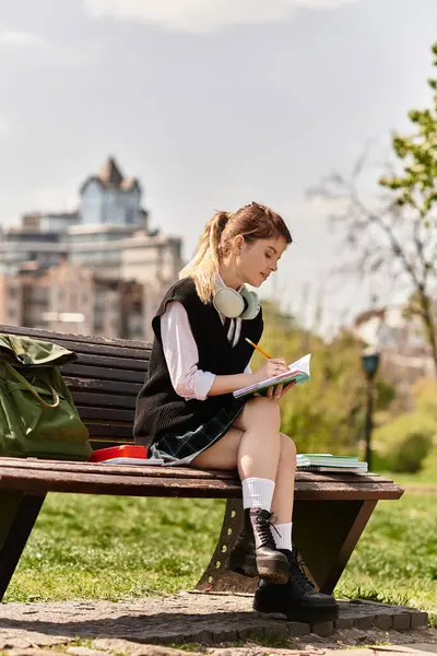Eine junge Studentin sitzt auf einer Bank und genießt die Sonne, während sie studiert und schreibt. — Stockfoto