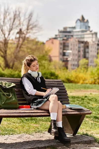 A young adult sits on a bench, absorbed in her studies, surrounded by nature on a beautiful day. — Stock Photo