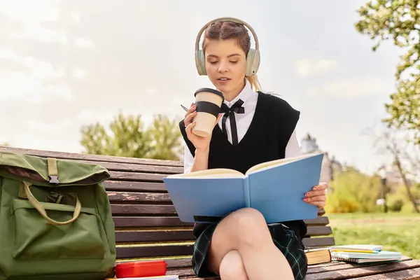 College girl sits on a park bench sipping coffee and reading a book in her stylish outfit. — Stock Photo