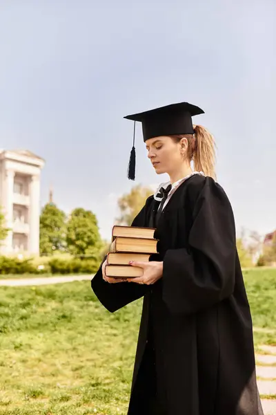 A young college student proudly dons her graduation cap and gown while holding books. — Stock Photo