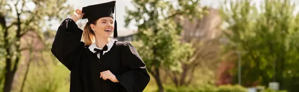 A young adult smiles brightly while celebrating her graduation outdoors under a clear sky, banner — Stock Photo