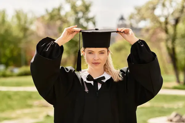 Jovem menina da faculdade ajusta seu boné de formatura enquanto abraça alegremente sua realização ao ar livre. — Fotografia de Stock
