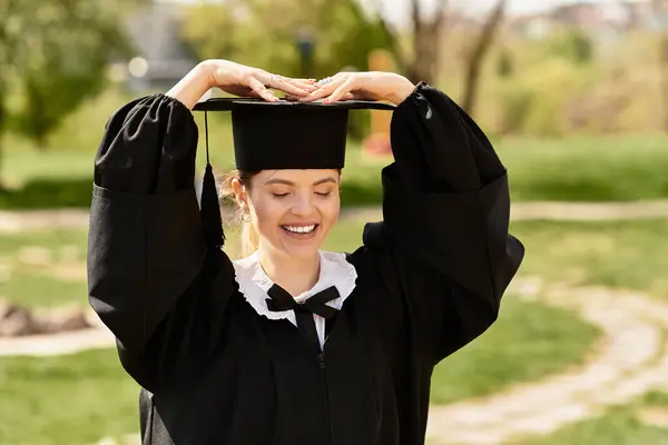 A joyful college girl in a graduation gown and cap celebrates her accomplishment outdoors. — Stock Photo