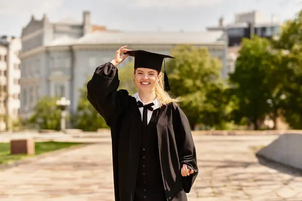 Joyful jovem adulto em vestido de graduação e boné orgulhosamente celebra realização ao ar livre na luz do sol. — Fotografia de Stock