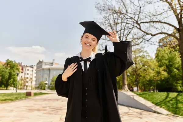 A bright young adult smiles radiantly while adjusting her graduation cap in a beautiful park. — Stock Photo