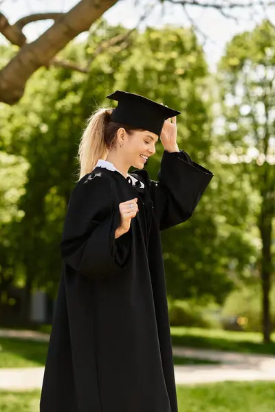 A college student joyfully adjusts her graduation cap while enjoying the sunny outdoors. — Stock Photo