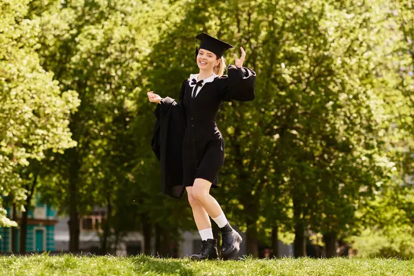 A joyful young adult in a graduation gown and cap celebrates her accomplishment outdoors. — Stock Photo