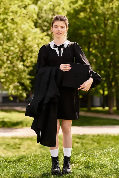A confident college girl holds her gown and cap, celebrating her graduation success. — Stock Photo