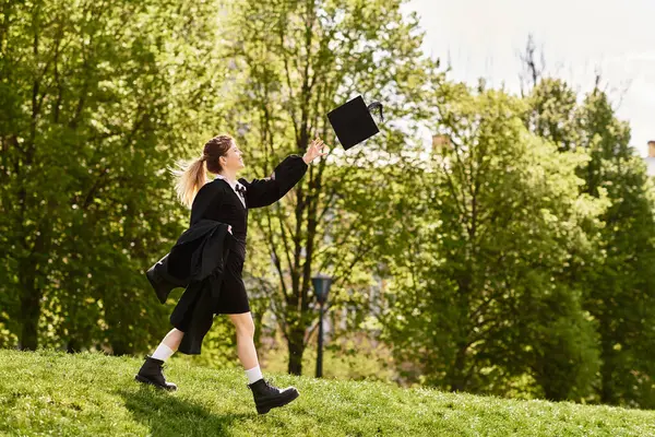 Una joven universitaria celebra la graduación lanzando su gorra al aire, rodeada de vegetación. - foto de stock