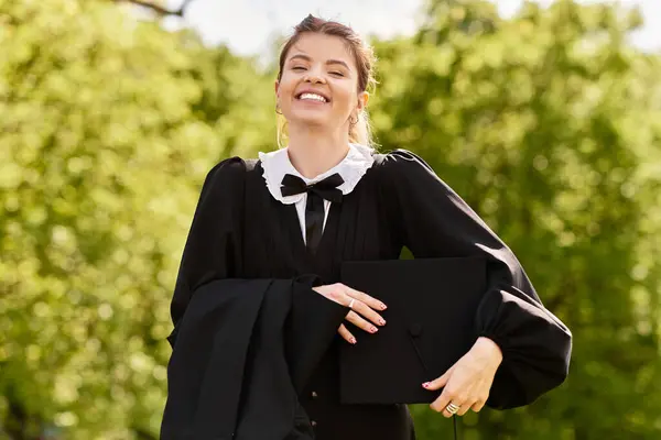 A college girl smiles in her graduation gown and cap, celebrating her achievement outdoors. — Stock Photo