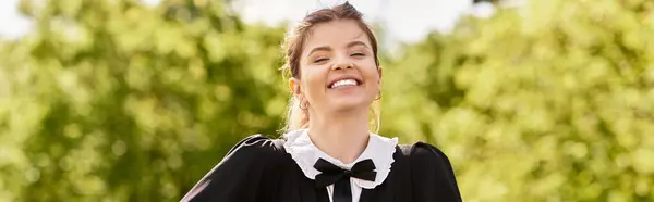 A young woman beams with happiness while dressed in her graduation gown and cap, banner — Stock Photo