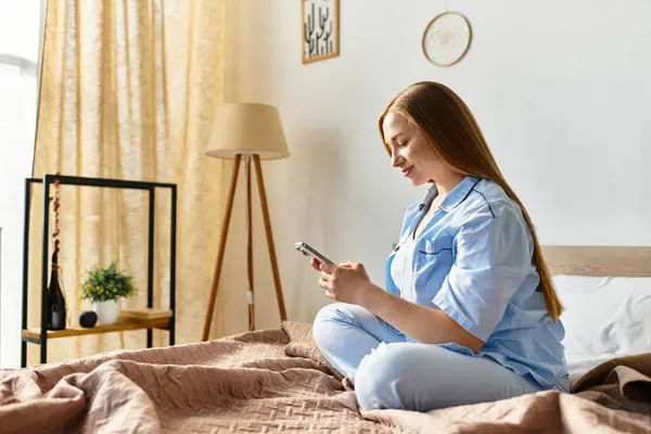 Une jeune femme s'assoit confortablement sur son lit, profitant d'un peu de temps personnel en utilisant son téléphone. — Photo de stock