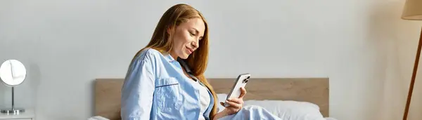 Young woman lounging in bed, relaxed and happy, scrolling through her smartphone in comfort. — Stock Photo
