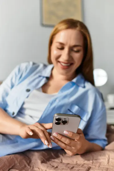 Warm light fills the room as a young woman smiles while using her smartphone, feeling at home. — Stock Photo